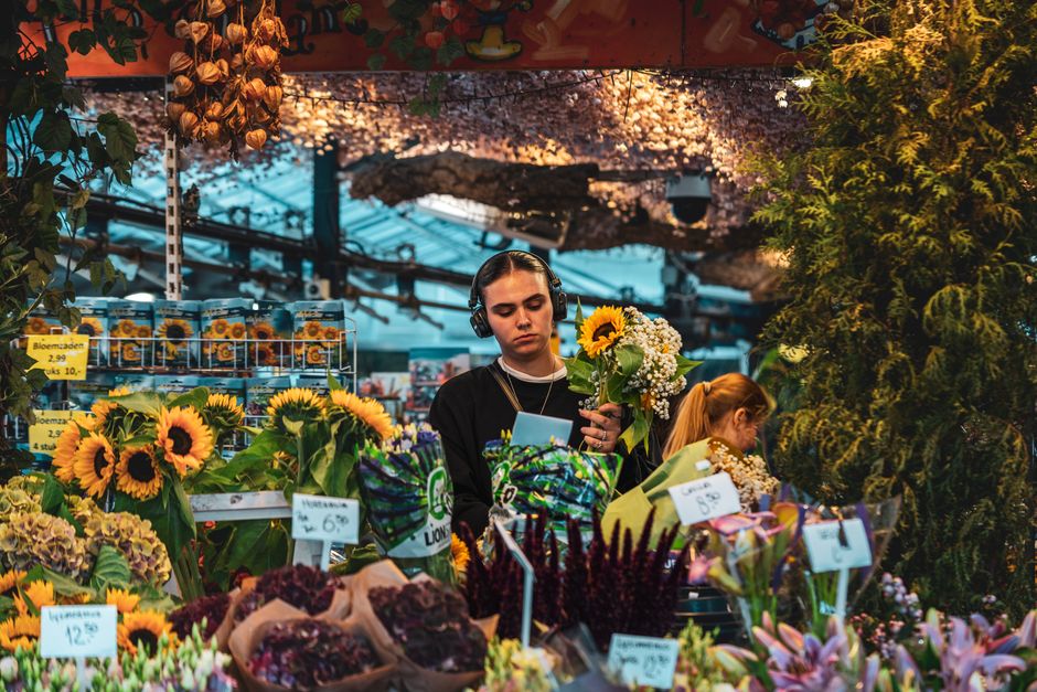 A young female florist at floristbethnalgreen.co.uk is arranging a floral gift consisting of bright yellow sunflowers and white baby's breath, currently holding the bouquet in her left hand while look